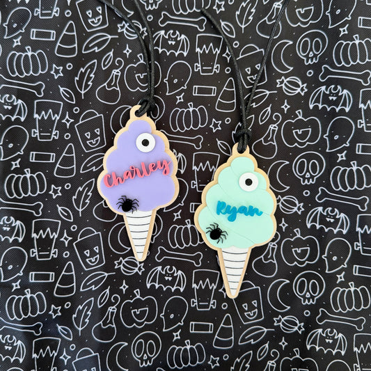 Two personalized ice cream cone charms with Halloween-themed names and spider accents, displayed on a black patterned background.